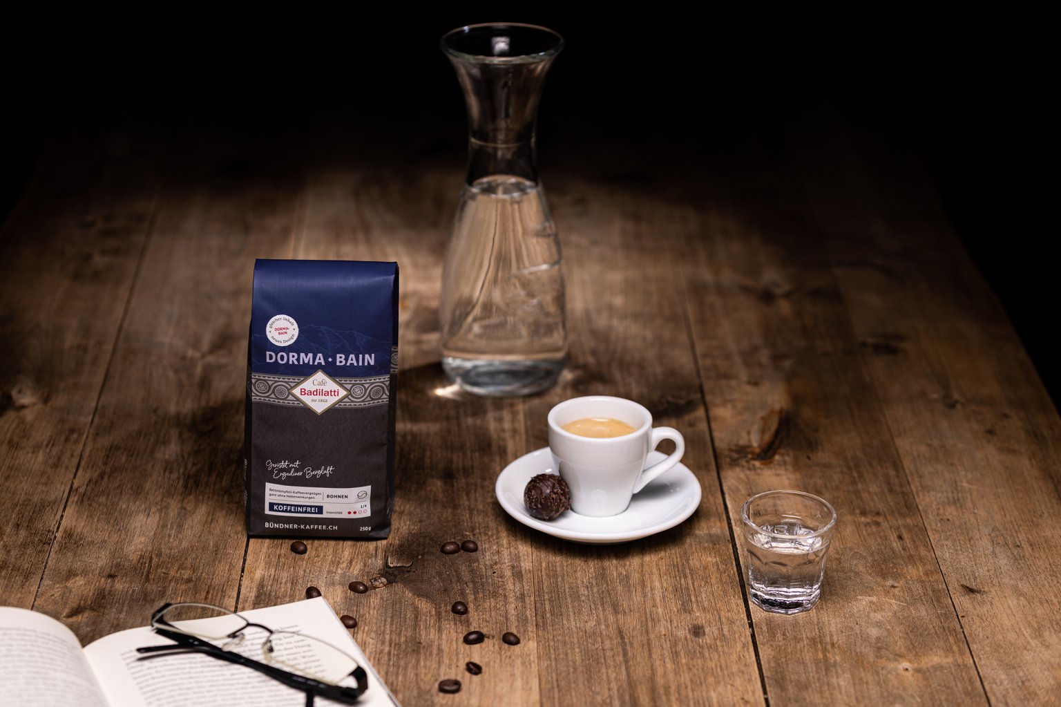 Koffeinfreier Espresso mit feiner Truffe-Praline, aufgeschlagenes Buch mit Lesebrille und Dorma Bain Kaffeebohnen von Cafè Badilatti.