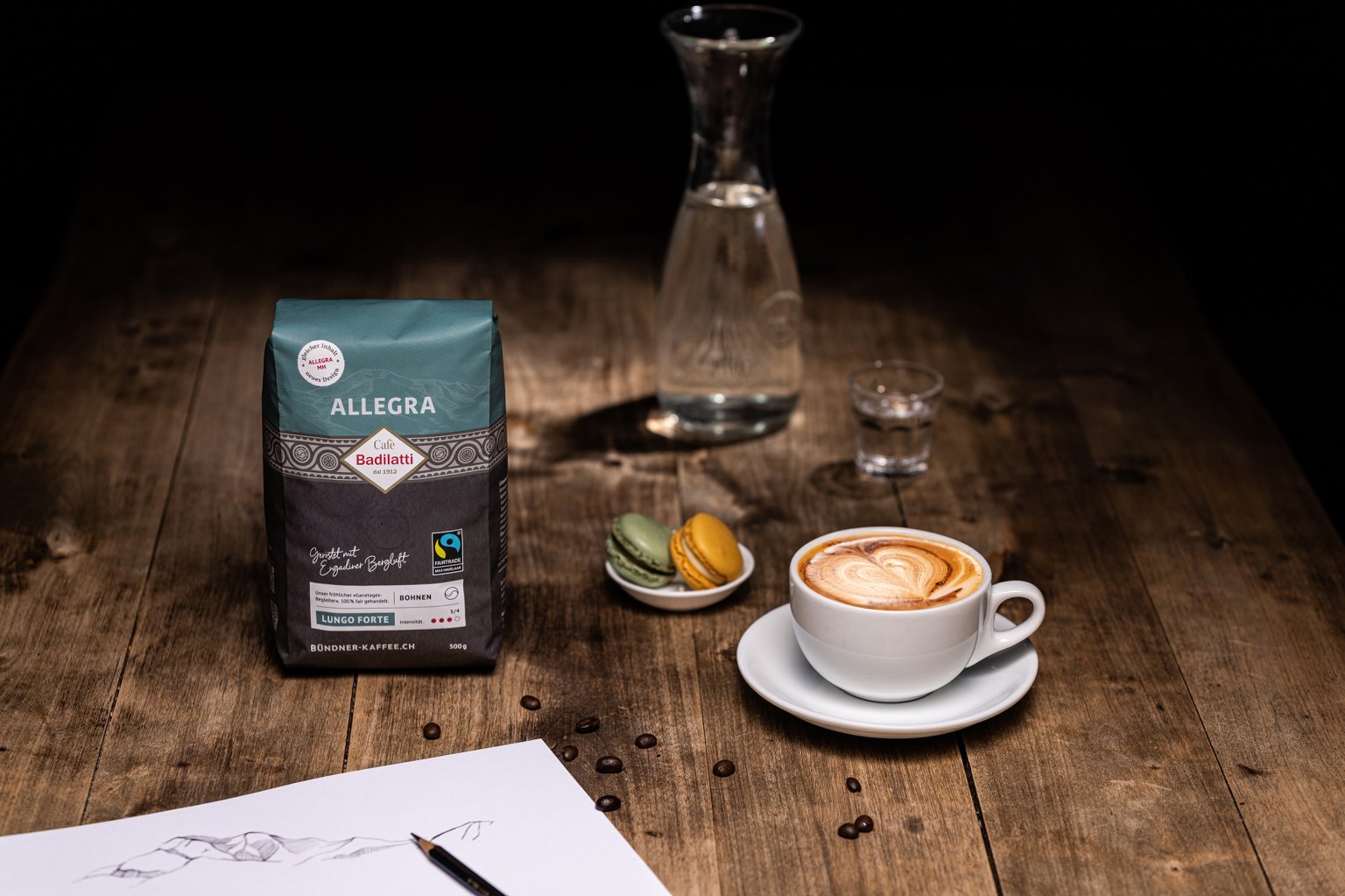 Cappuccino, Macarons, eine Bleistiftzeichnung und Allegra-Bio Kaffeebohnen von Cafè Badilatti.